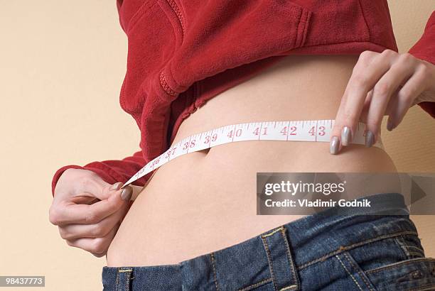 young woman measuring her waistline - anorexia nervosa stock pictures, royalty-free photos & images