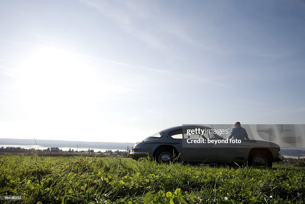 Bald man standing on meadow by his classic car watching landscape