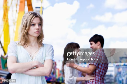 Sulking teenage girl at fun fair with couple in background Sulking teenage girl at fun fair with couple in background