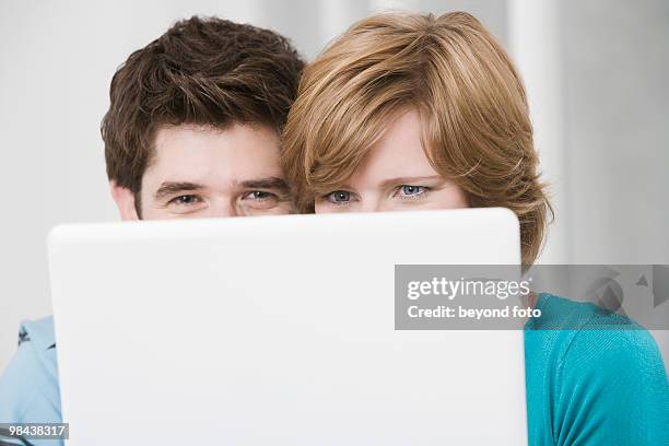 young couple hiding behind laptop computer - hiding behind laptop stock pictures, royalty-free photos & images