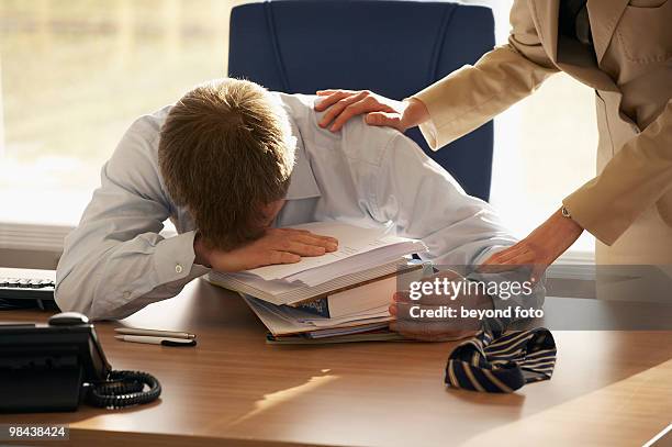 stressed businessman at his desk being helped by female colleague - beca stock-fotos und bilder