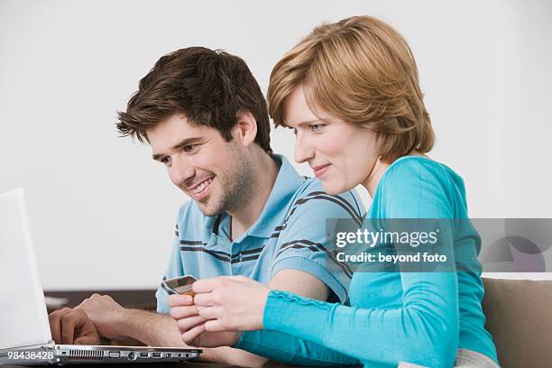 young couple in front of laptop computer with credit card - bavarian man in front of house stockfoto's en -beelden