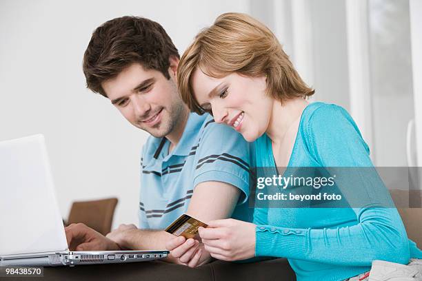 young couple in front of laptop computer with credit card - bavarian man in front of house stockfoto's en -beelden