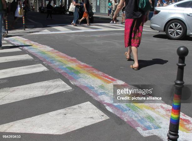 June 2018, France, Paris: A woman walks along a rainbow, which was covered with paint at a street crossing. Shortly before a so-called pride parade...
