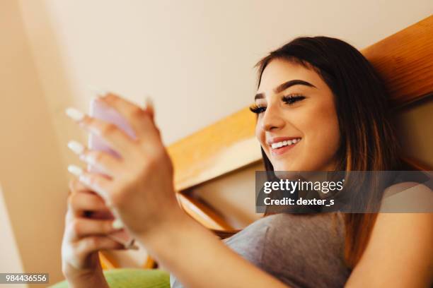 teenage girl lying in bed and looking at her mobile phone - dexters stock pictures, royalty-free photos & images