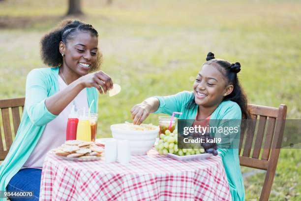 african-american mother and daughter eating potato chips - family eating potato chips stock pictures, royalty-free photos & images