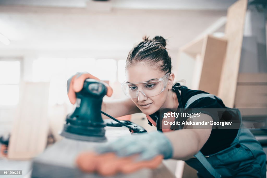 Female Craftswoman Sanding Wooden Log For Manufacturing Furniture