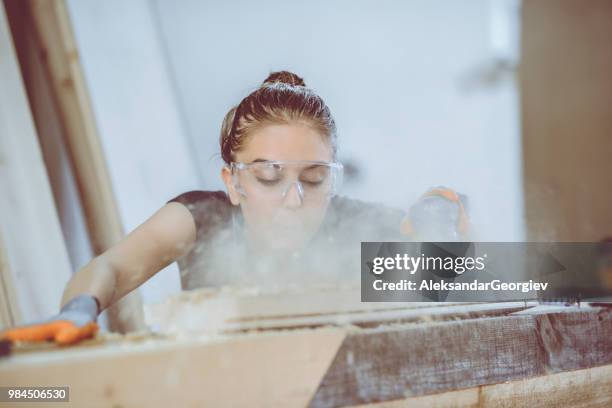 süße weibliche tischler schleifen und bläst staub von der planke - sägemehl stock-fotos und bilder