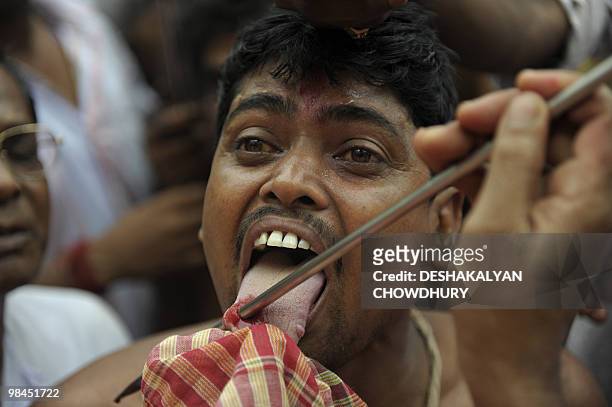 An Indian Hindu devotee reacts as a priest pierces his tongue with a metal rod during the ritual of Shiva Gajan at a village in Bainan, some 80 kms...