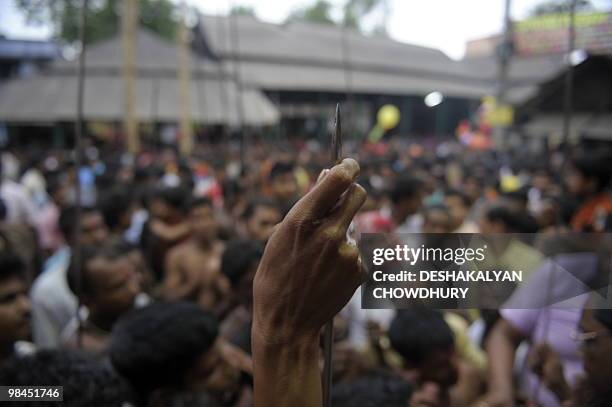 An Indian Hindu devotee polishes the tip of a metal rod before using it to pierce his tongue during the ritual of Shiva Gajan at a village in Bainan,...