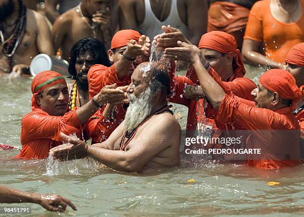 Followers of a Hindu Sadhu pour water over his head as they bathe in the river Ganges during the Kumbh Mela festival in Haridwar on April 14, 2010....