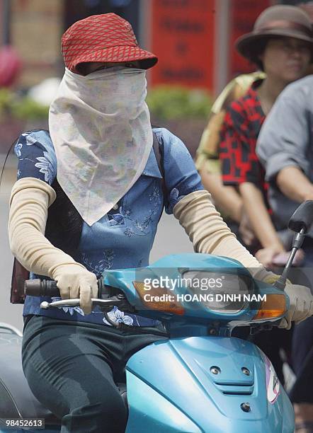 Masked woman wearing long gloves rides a motorcycle on a Hanoi street, 13 June 2003. Today, as has been the case for centuries, beauty in the minds...