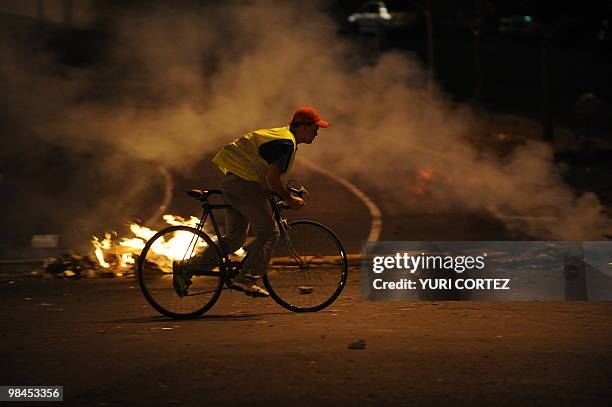 Man rides his bike next to a barricade on fire in a blocked street in front of the University of Costa Rica on April 13, 2010 during a protest...