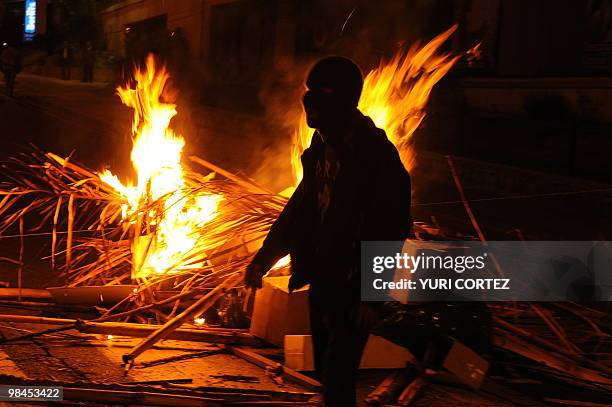 Masked university student walks past a barricade on fire in a blocked street in front of the University of Costa Rica on April 13, 2010 during a...