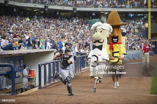 Colorado Rockies Paul Phillips trying to avoid mascots: Paco the Chorizo, Brett Wurst the Bratwurst, and Guido the Italian Sausage on field during...