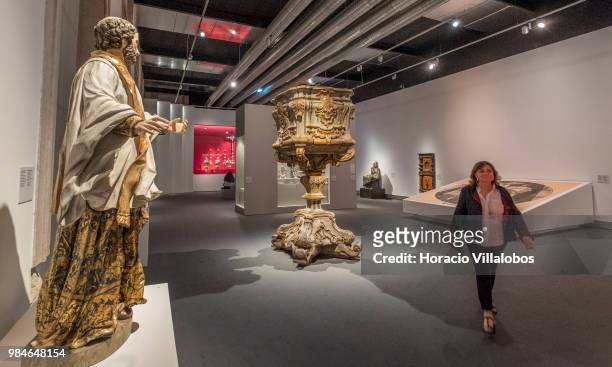 Woman walks by religious furniture and figures on display at "Na Rota Das Catedrais - Construcoes E Identidades" exhibition in D. Luis I gallery of...