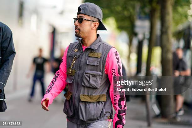 Guest wears a gray cap, a pink CDG Comme des Garcons pullover, a sleeveless tactical jacket, outside 1017 ALYX 9SM, during Paris Fashion Week -...