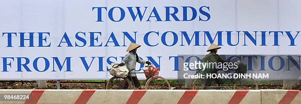 Two recyclable-items collectors walk past a poster marking the 16th summit of the Association of Southeast Asian Nations on a road in Hanoi on April...