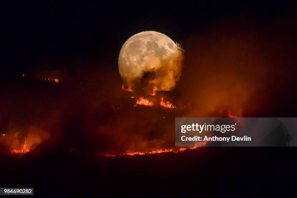 The full moon rises behind burning moorland as a large wildfire sweeps across the moors between Dovestones and Buckton Vale in Stalybridge, Greater...