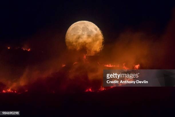 The full moon rises behind burning moorland as a large wildfire sweeps across the moors between Dovestones and Buckton Vale in Stalybridge, Greater...