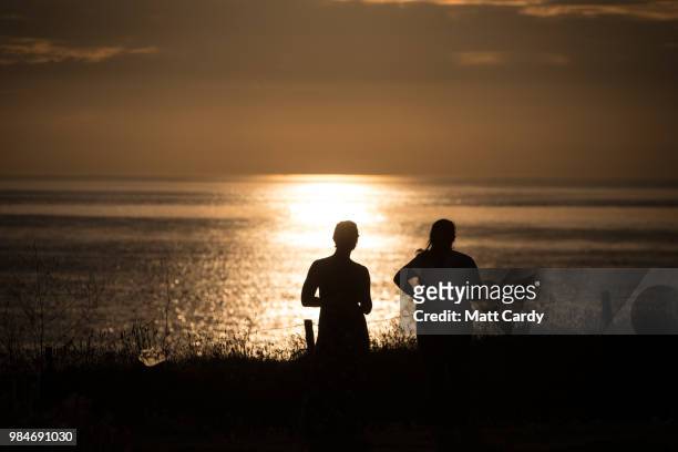 People watch the sun set as they enjoy the fine weather at Godrevy Lighthouse near Gwithian on June 26, 2018 in Cornwall, England. Parts of the UK...