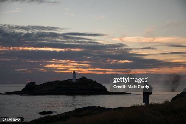 People watch the sun set as they enjoy the fine weather at Godrevy Lighthouse near Gwithian on June 26, 2018 in Cornwall, England. Parts of the UK...