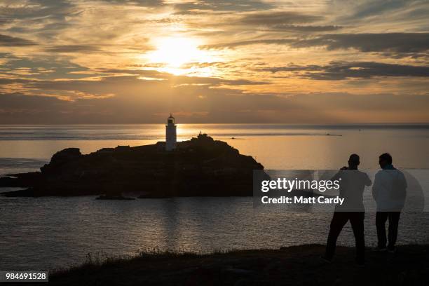 People watch the sun set as they enjoy the fine weather at Godrevy Lighthouse near Gwithian on June 26, 2018 in Cornwall, England. Parts of the UK...