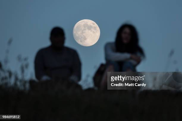The moon rises behind people sat overlooking sun Godrevy Lighthouse near Gwithian on June 26, 2018 in Cornwall, England. Parts of the UK are...