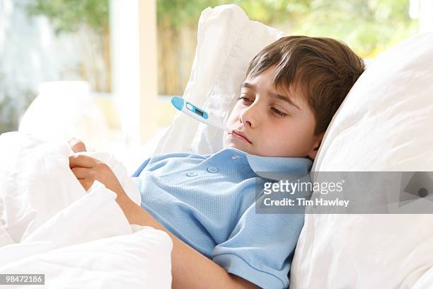 boy in bed with thermometer in mouth - im mund tragen stock-fotos und bilder