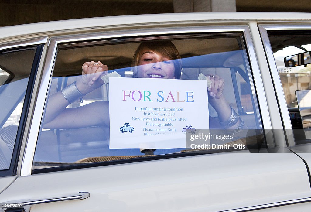 Young woman pasting 'For Sale' sign on her car