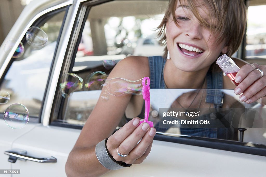 Young woman blowing bubbles out a car window