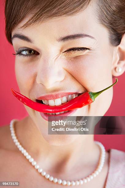 young woman biting on red chilli, winking - carrying in mouth ストックフォトと画像