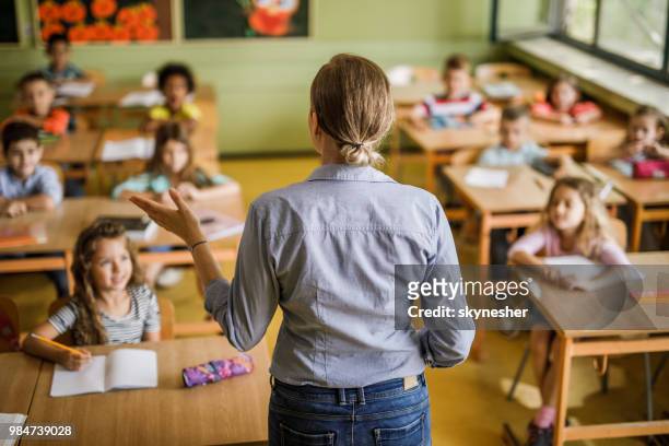 rear view of a female elementary teacher giving a lesson in the classroom. - elementary school building stock pictures, royalty-free photos & images
