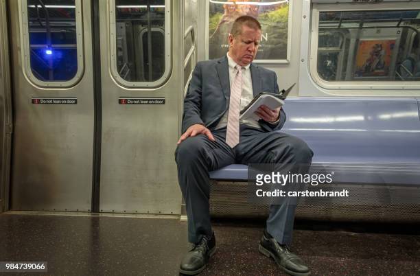 hombre sentado en un tren de metro leyendo en una revista - manhattan magazine fotografías e imágenes de stock