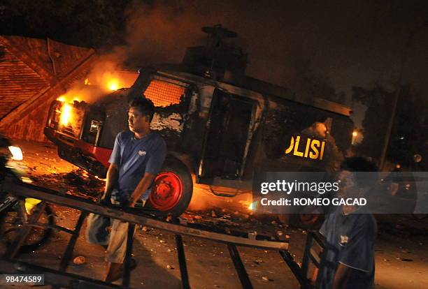 Residents salvage scraps while a police water canon truck burns after some 70 police vehicles were torched by demonstrators during clashes with...