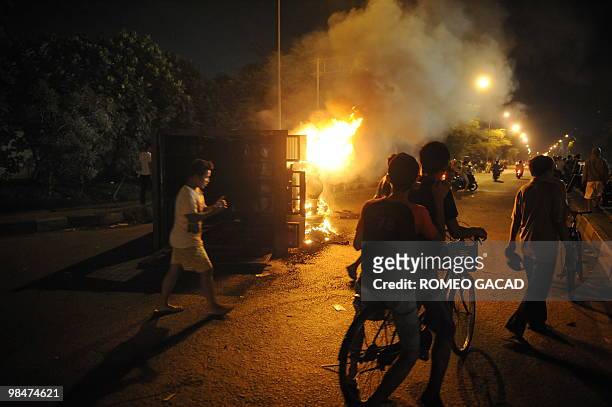 Residents pass by a police van in fire after some 70 police vehicles were torched by demonstrators during clashes with police near a cemetery outside...