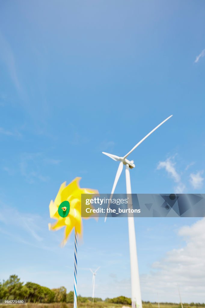 Yellow pinwheel toy and wind turbine against sky