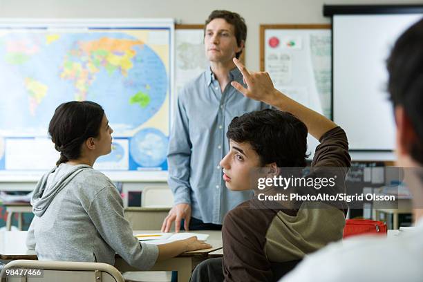 high school student raising hand in class, looking over shoulder - boy looking over shoulder stock pictures, royalty-free photos & images