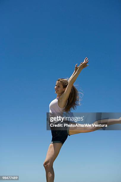 young woman with arms raised, balancing on one leg - legale stockfoto's en -beelden
