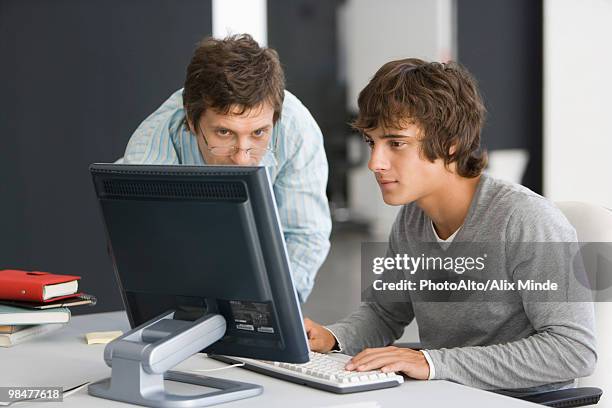 teacher assisting student with computer assignment - teacher bending over stock-fotos und bilder