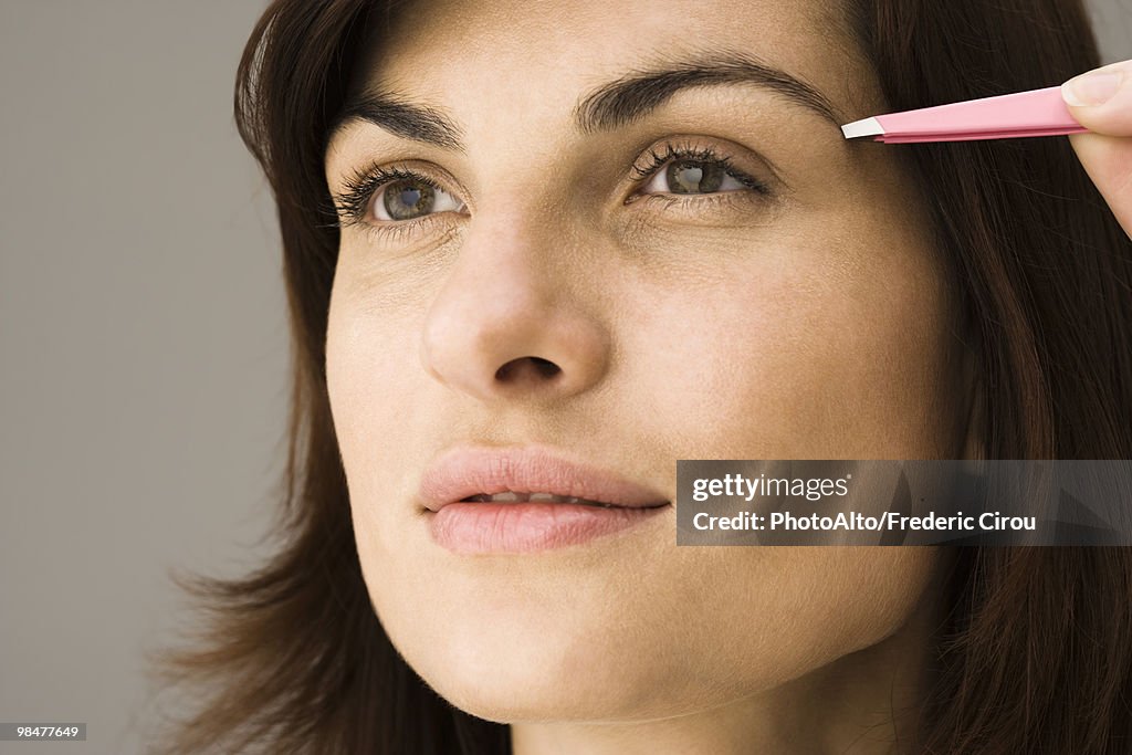 Young woman tweezing eyebrows