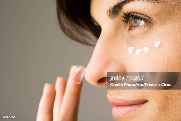 young woman applying undereye cream - faltenreduktion stock-fotos und bilder
