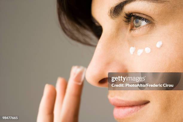 young woman applying undereye cream - antiarrugas fotografías e imágenes de stock