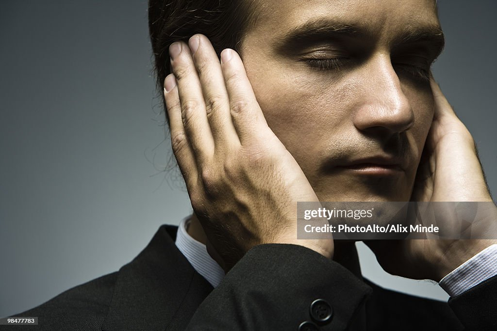 Man with hands held over ears and eyes closed