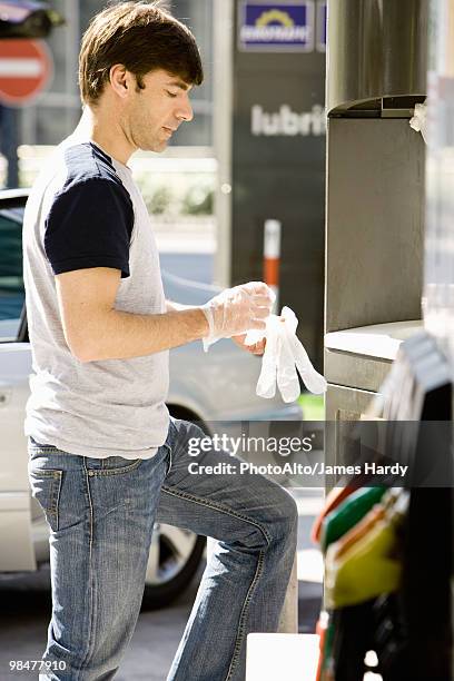 man at gas station puttong on disposable gloves preparing to refuel vehicle - homens de idade mediana imagens e fotografias de stock