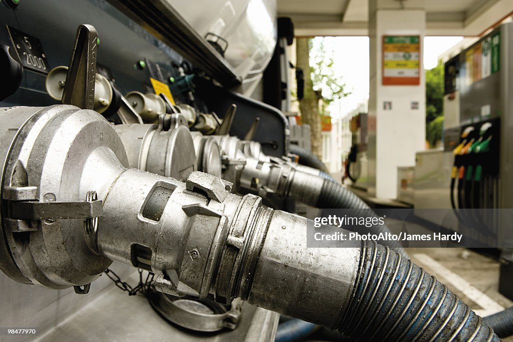 Hoses connected to fuel tanker outlets transferring fuel to gas station storage tanks