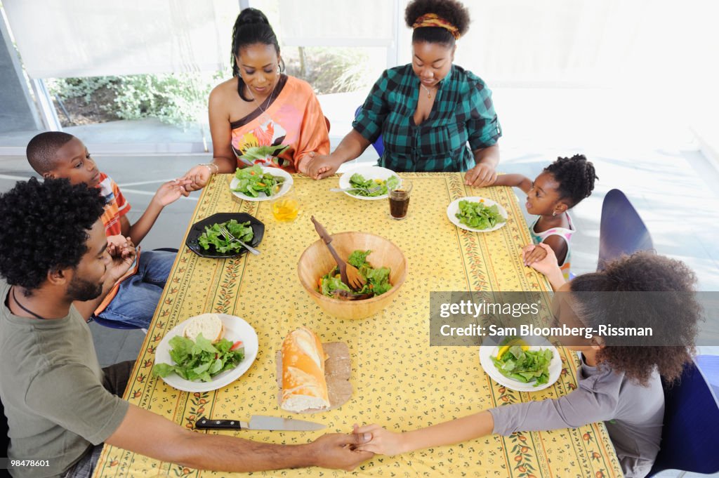 Black family saying grace at dining room table