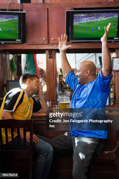 cheering men watching television in sports bar - rivaliteit stockfoto's en -beelden