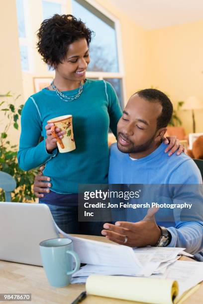 african american husband paying bills as wife watches - jon feingersh stock pictures, royalty-free photos & images