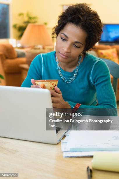 mixed race woman drinking coffee and paying bills online - jon feingersh stock pictures, royalty-free photos & images